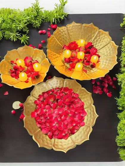 A set of three golden hammered metal bowls, displayed here as decorative urlis filled with flowers and floating candles. These versatile bowls are perfect for festive centerpieces in an office or as a beautiful corporate gift.