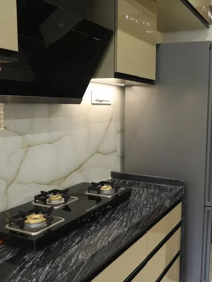 A close-up of a kitchen with a black granite countertop and a modern chimney. The under-cabinet lighting provides excellent task lighting for cooking.