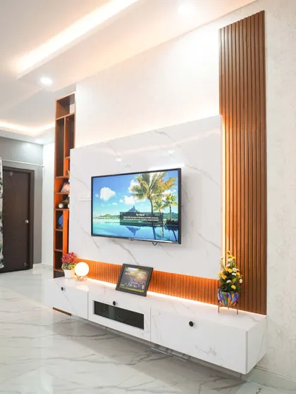 This modern living room features a floating TV unit with a white marble-finish back panel and fluted wooden accents. The warm, indirect lighting creates a cozy and sophisticated ambiance for entertainment.