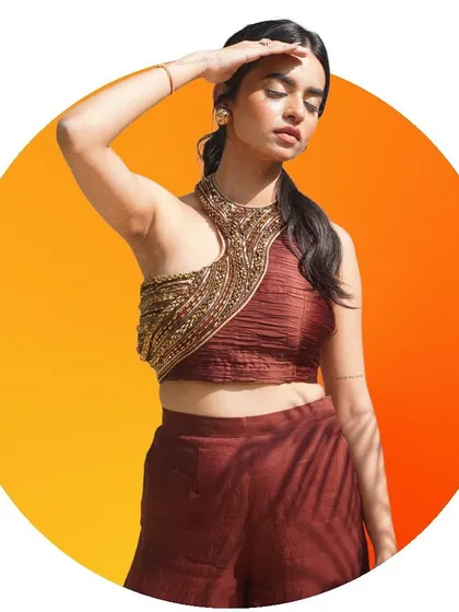 A creative, graphic-style portrait featuring a model in a contemporary ethnic top with a heavily beaded neckline, set against a vibrant orange circle.