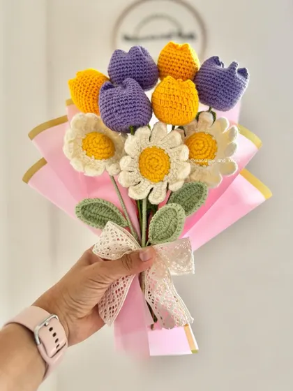 Holding a finished custom bouquet of crochet tulips and daisies. The pink wrapping paper and lace bow complete this special birthday gift.