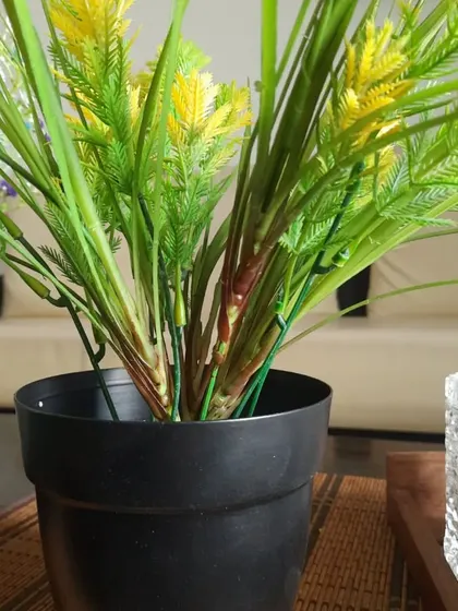 A basic black plastic pot with a lush yellow artificial plant. This shows that even simple planters can look great with the right plant choice.