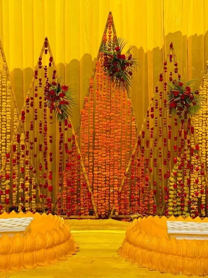 A traditional Haldi seating area, with a backdrop made of marigold and rose petal strings in geometric patterns.