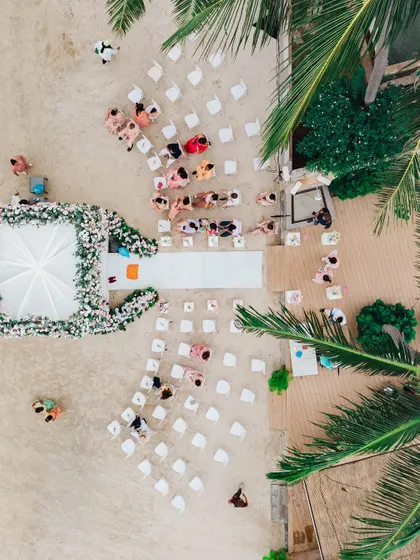 An aerial drone shot of a beach wedding ceremony in Thailand. This perspective shows the beautiful layout of the event, with the guests seated on the sand and the elegant mandap positioned right by the water's edge.