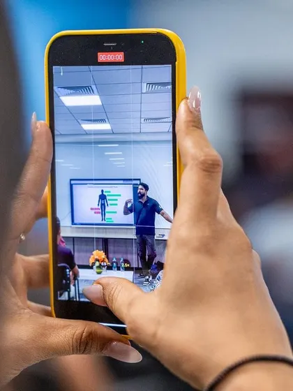 A participant captures a moment from a presentation on their phone, saving key insights from the 2024 UKSCA conference.