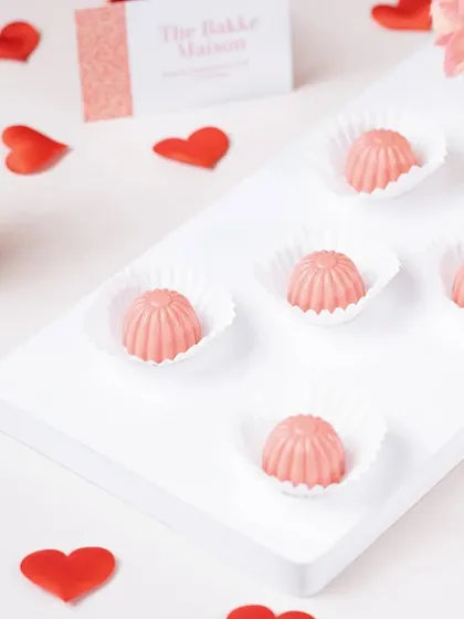 Pink bonbons arranged on a clean white surface with heart confetti. This minimalist and romantic styling is perfect for Valentine's Day confectionery.