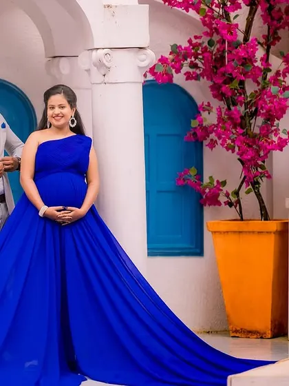 The vibrant bougainvillea and Santorini-style architecture provide a beautiful, colorful backdrop for this maternity photo. The royal blue of the gown stands out against the white and blue walls.