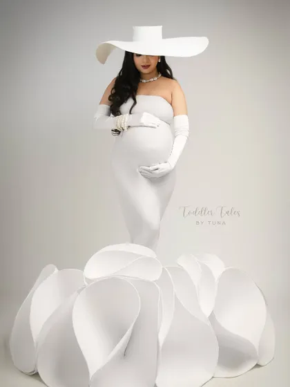 A frontal view capturing the full bloom effect of the gown. The mother cradles her bump, a picture of grace and anticipation, enveloped in petals.