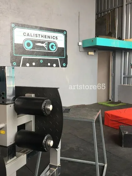 The finished 'Calisthenics OG' cassette tape mural in its gym setting. This type of graphic wall art is perfect for creating photo opportunities and reinforcing the brand identity of a fitness space.