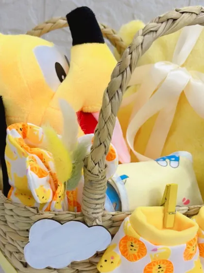 This detailed view inside the newborn welcome basket shows the soft yellow blanket, a Pluto plush toy, and a set of comfortable baby clothes, all packed and ready for gifting.