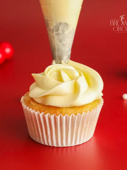 A close-up of our vanilla cupcake getting its swirl of frosting. This simple, elegant cupcake is a perfect canvas for festive decorations and is a popular choice for gifting.