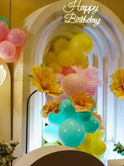A full view of the rainbow floral garden theme. The combination of colorful paper flowers, balloons, and lit floral floor lamps creates a vibrant and joyful setting for a birthday party.