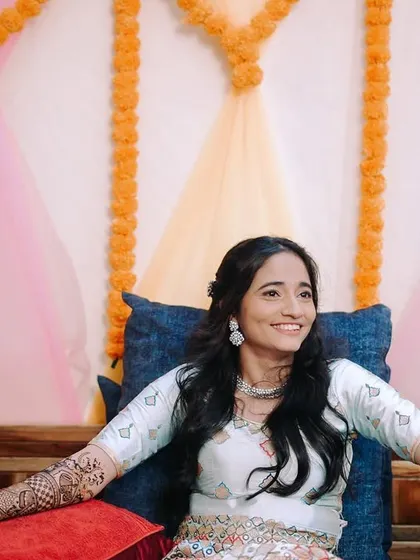 A candid shot of the bride smiling as her mehndi is being applied, with her family around her. It captures the relaxed and happy atmosphere of the event.