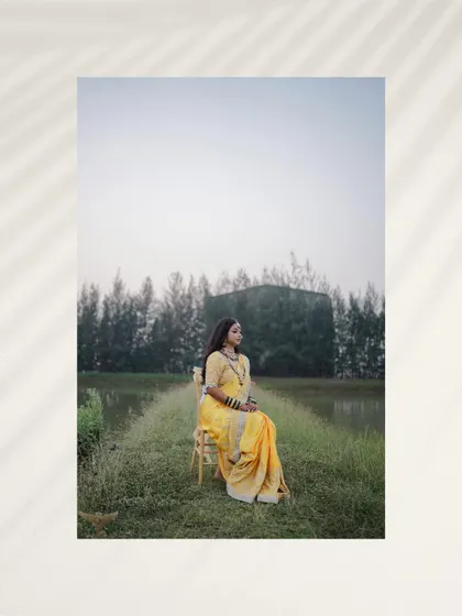 A portrait that captures the tranquility of the countryside. The bride is seated in a field, her vibrant yellow saree a beautiful pop of color against the green, rustic landscape.