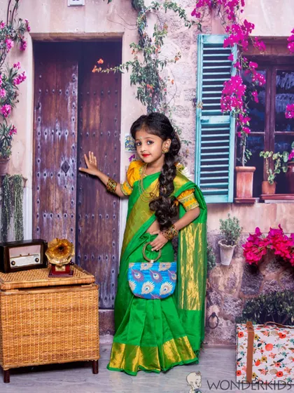 A young girl dressed in a beautiful green pattu pavadai, posing elegantly in a charming European street-themed setting. The combination of traditional wear and a unique backdrop creates a stunning photo.