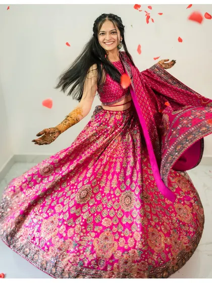 The bride twirls in her vibrant pink lehenga, showering rose petals during her Mehendi celebration.