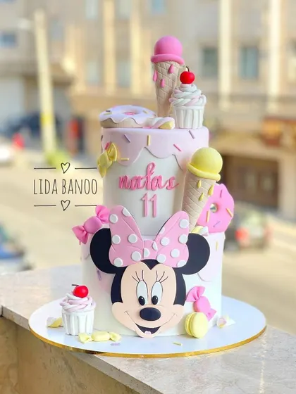 A fun and sweet Minnie Mouse cake for an 11th birthday. This two-tiered cake is topped with ice cream cones, donuts, and cupcakes, combining two favorite treats in one.