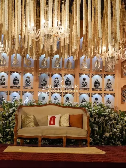 A classic reception stage featuring a backdrop of traditional Indian 'jharokha' niches, framed by a ceiling of hanging white floral strings for a delicate, elegant look.
