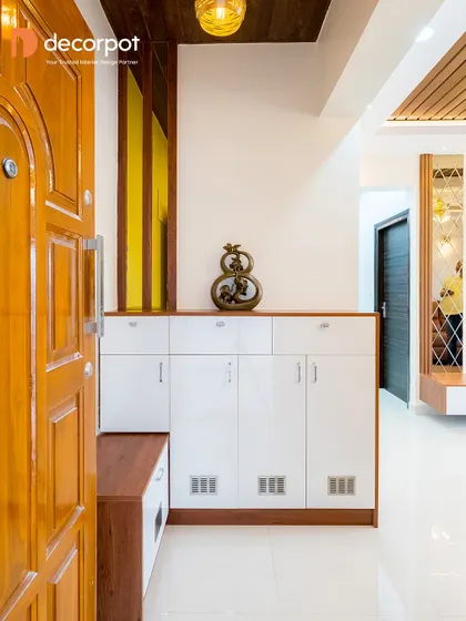 A bright and functional foyer design with a white high-gloss shoe cabinet that includes a built-in wooden seater. The yellow fluted panel adds a pop of color and texture to the entryway.