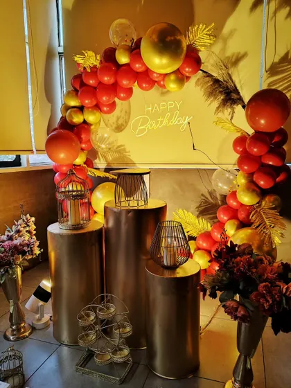 A stylish indoor setup with gold pedestals and a red and gold balloon arch, perfect for a sophisticated birthday party.