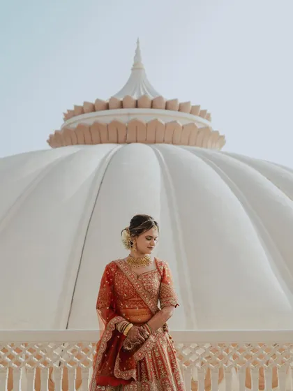 A stunning bridal portrait against the grand white dome of Indana Palace. The architectural symmetry and the bride's elegant pose create a powerful and regal image.