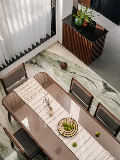 **The Glow House, Ahmedabad:** An overhead view of the dining area highlights the rich texture of the green marble flooring. The simple, elegant furniture allows the natural materials to be the focus, creating a space that is both sophisticated and grounded.