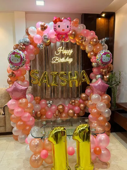 A Hello Kitty theme for an 11th birthday, featuring a circular balloon arch in pink and rose gold with the birthday girl's name in foil letters.