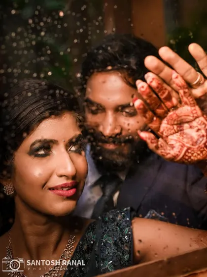 A creative and artistic shot of a couple through a rain-streaked window, with the bride's hennaed hand on the glass.