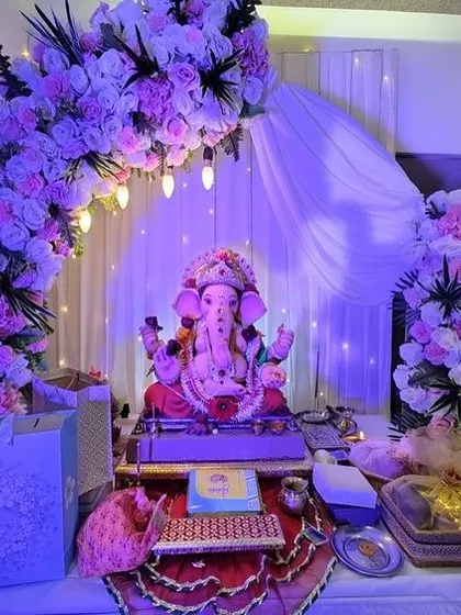 A beautiful floral arch in shades of lavender and white, with a soft white drape as a backdrop. The purple lighting enhances the color scheme and creates a serene, evening-ready look.