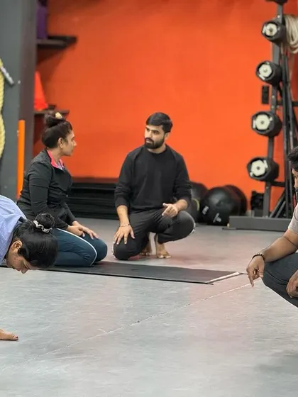 Personal training with us means getting detailed, one-on-one attention. Here, our trainers are observing a client's form in a forward fold, providing corrections to ensure she gets the most out of the stretch safely. This personalized guidance is key to achieving specific fitness and recovery goals.