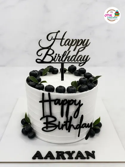 A classic and elegant blueberry birthday cake. The clean, white-ribbed buttercream is topped with a crown of fresh blueberries and personalized with a modern black acrylic topper.