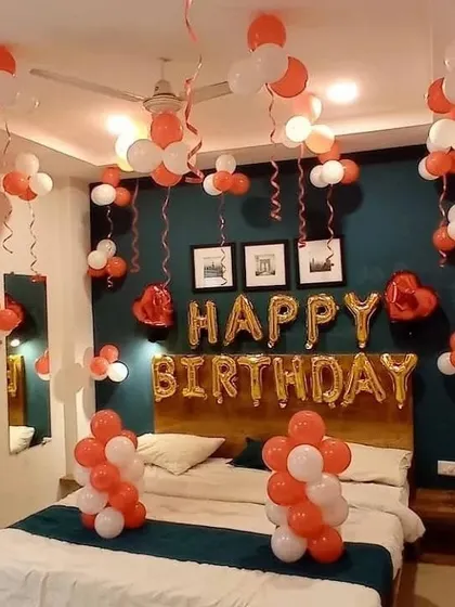 A lovely bedroom decoration in orange and white, with balloon clusters and a "Happy Birthday" foil banner over the bed.