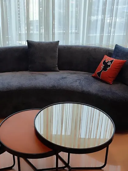 A gracefully curved sofa upholstered in a deep, plush black fabric, providing a dramatic anchor to the living space. The addition of a single, vibrant red cushion with a graphic cat motif adds a playful and personal touch, highlighting our custom cushion design service.