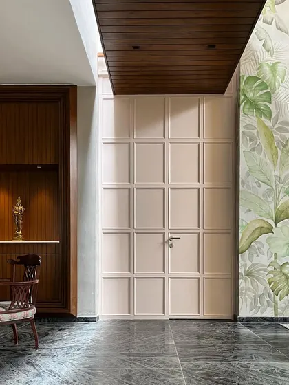 Detail of the paneled door and puja niche. The design combines rich wood paneling, a custom mural, and dark marble flooring, showcasing a blend of textures and materials.