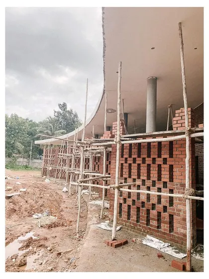 The curved brick facade of the auditorium taking shape, supported by traditional bamboo scaffolding. This image highlights the blend of modern concrete forms with traditional building materials and techniques.