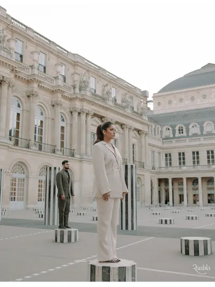 A wide-angle view of the couple at the Palais Royal, emphasizing the grandeur of the location and creating a sense of fashionable isolation.