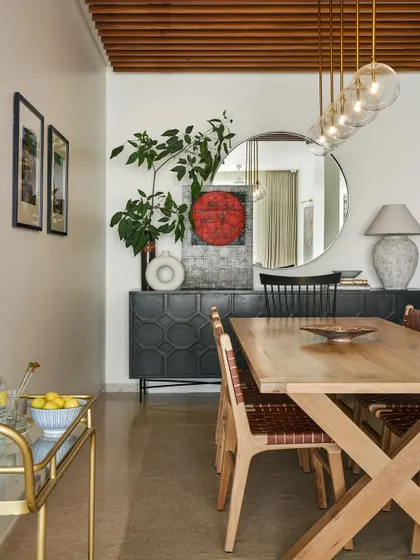 A modern dining room with a rustic touch. The live-edge wood table is paired with leather-woven chairs, while a large round mirror reflects light and makes the space feel larger.