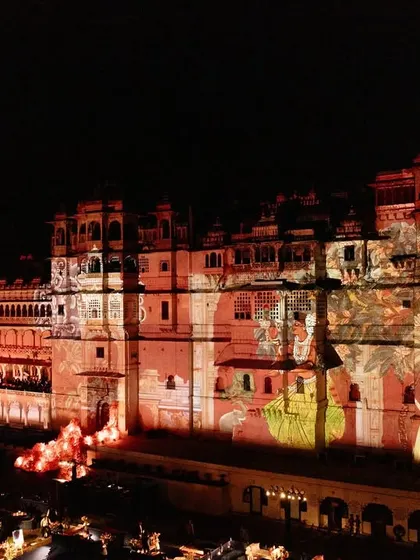 A wide shot of the Udaipur city palace, its entire facade lit up with intricate projection mapping for a spectacular Sangeet backdrop.