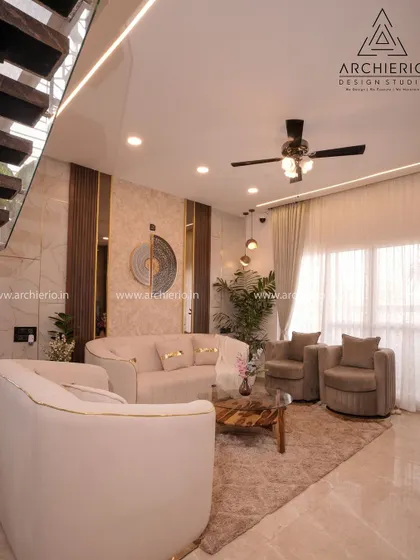 A luxurious living room in a duplex villa, featuring a floating staircase and high ceilings. The design uses a neutral palette and sophisticated furniture to create a grand and airy space.