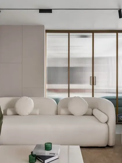 This angle highlights the architectural elements we use to define space. A frosted glass partition with a golden frame separates the living area while allowing light to flow through, maintaining an open feel. The clean lines of the wall paneling add texture and depth.