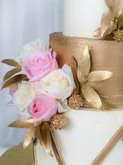 A close-up of the 'Golden Whispers of Love' cake, showing the detail of the brushed gold tier, the fresh roses, and the golden leaves. This design is perfect for a glamorous and modern wedding.
