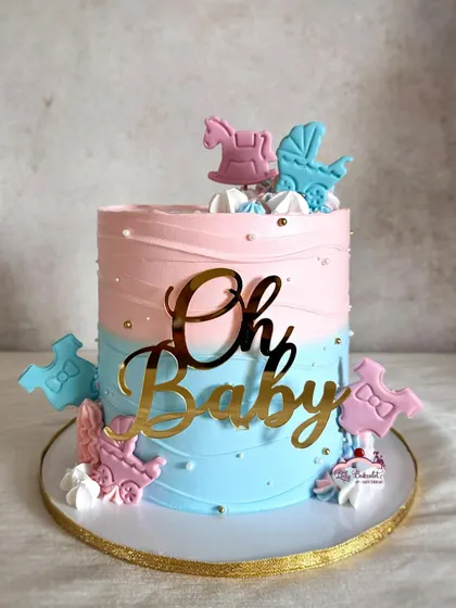 A classic "Oh Baby" shower cake in pink and blue, decorated with cute edible baby-themed toppers like rocking horses and onesies.