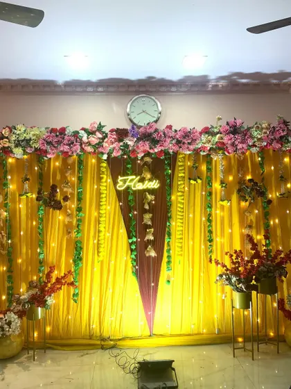 A full view of the yellow and maroon Haldi backdrop. The combination of colors, lights, and flowers creates a rich and festive atmosphere for a home celebration.