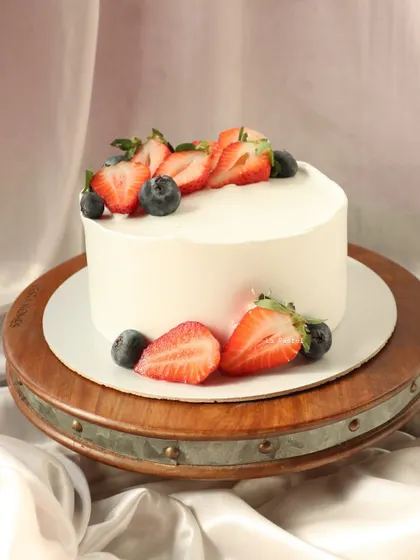 A simple and fresh vanilla cake topped with sliced strawberries and blueberries.