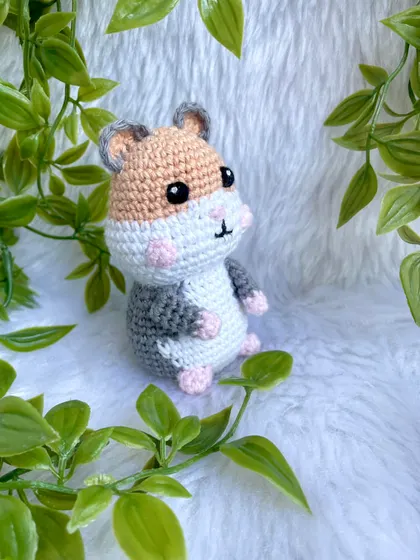 The crochet hamster sitting among some greenery.