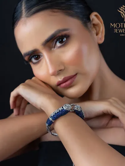 A bold statement bangle featuring two stylized animal heads encrusted with blue sapphires and diamonds. This is a powerful and artistic piece for the confident jewellery connoisseur.