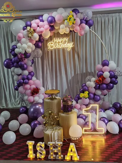 A first birthday party decoration with a purple, pink, and white balloon ring with floral accents.