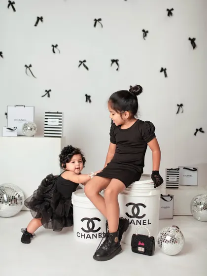 Big sister helps her little sister stand, a sweet moment of support amidst the high-fashion fun.
