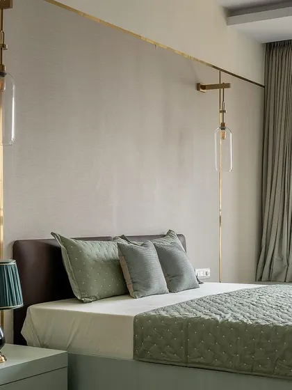 A bedroom where lighting is the star. Custom brass wall sconces stretch across the textured wall, providing both ambient and reading light, while the sage green color palette promotes a sense of tranquility.