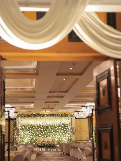 A glimpse into the Nikah ceremony hall through the elegantly decorated entrance, showing the beautiful white floral stage in the distance.